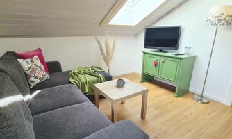 A cozy living room with a gray sofa and a green sideboard. A television and a bright ceiling create an inviting atmosphere.