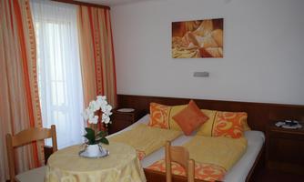A cozy room with a large double bed and colorful decorations. A table with a flower complements the inviting atmosphere.