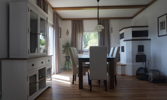 A bright dining area with a large table and elegant chairs. The room has large windows that let in plenty of daylight, and a cozy corner with a fireplace.