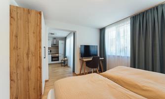 A modern bedroom with two beds and a large window. The room has a minimalist style with wood and gray tones.
