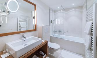 A modern bathroom with a bathtub and a washbasin. Bright tiles and a large mirror lighting create a pleasant atmosphere.