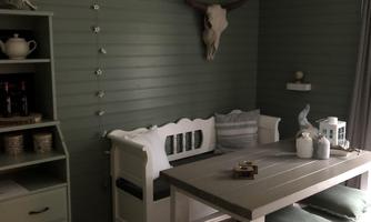 A cozy dining area with a white bench, a large table, and soft green walls. A stylish ceiling lamp and a deer antler add character to the room.