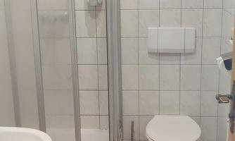 A modern bathroom with a shower enclosure, a toilet, and a sink. The floor is covered with wooden planks, and there is a towel on the floor.
