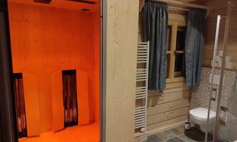 A modern bathroom with an infrared sauna. The walls are made of wood, and there is a window as well as a shower and toilet.