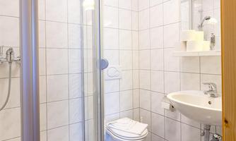 A modern bathroom with a shower cabin and a sink. The walls are tiled, and the floor has a blue and white pattern.