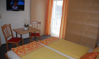 A cozy bedroom with two beds and warm colors. A table with chairs and a television in the background complete the room.