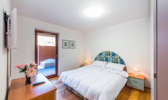 A cozy bedroom with a large bed and a wooden floor. The room has a window with access to a small balcony.