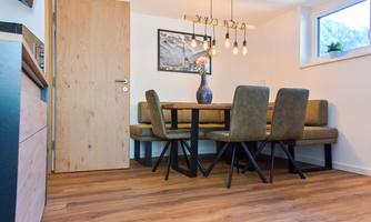 A modern dining room with a wooden table and comfortable chairs. Hanging lamps and a window create a bright, inviting atmosphere.