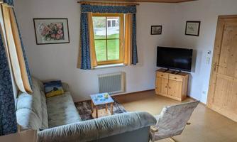 A cozy living room with a sofa, a television, and a small table.  
Large windows let in plenty of light and offer a view of the outdoors.