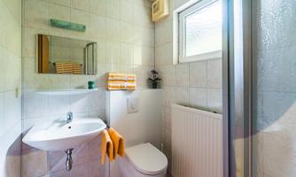 A bright and modern bathroom view with a shower, sink, and a toilet. Towels are neatly placed on a shelf.