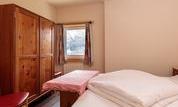 A simple bedroom with a bed and a wooden wardrobe. A window provides daylight and a calm atmosphere.