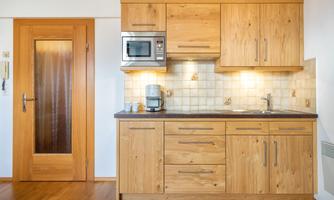 Modern wooden kitchen with space for appliances and plenty of storage. The wall tiles are bright and the lighting creates a pleasant atmosphere.