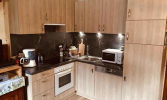 A modern kitchen with wooden cabinets and a dark countertop. It includes appliances such as a stove, a microwave, and a kettle.