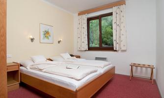 A cozy bedroom with two beds and a large window. The walls are painted in soft colors, and there is a small table.