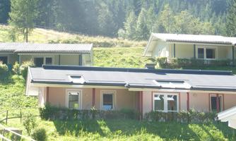Two modern houses in a green, wooded environment. The buildings are surrounded by a gentle hill, creating a calm and relaxed atmosphere.