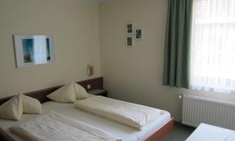 A simple and bright room with two single beds and minimalist decoration. Large windows provide plenty of daylight.