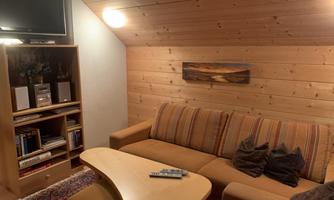 A cozy living space with bright wood interiors. A comfortable couch and a television are visible, as well as a bookshelf and a decorative mural.
