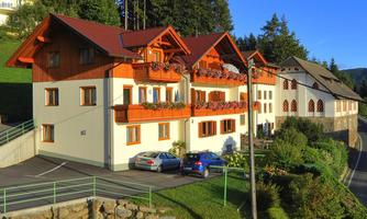 A picturesque house in alpine style with balconies and blooming plants. The surroundings are green and wooded, ideal for a peaceful stay in nature.