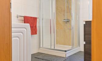 A modern bathroom with a glass shower and a functional laundry area. The walls are tiled in light colors, and a red towel provides a color accent.