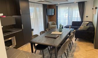 A modern kitchen-living room with a large dining table and elegant chairs. The space is bright and friendly, with large windows and stylish furniture.