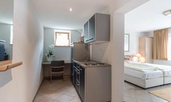 A modern kitchenette with a seating area. The room is bright and equipped with large windows.