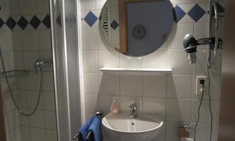 A modern bathroom with a round mirror and a sink. The walls are tiled, and towels hang next to each other.