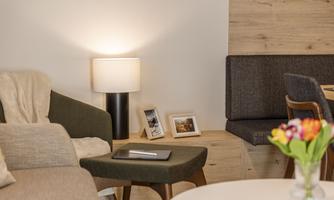 A cozy living room with a comfortable armchair, a lamp, and a small table. On the table lies a tablet, and fresh flowers adorn the surroundings.