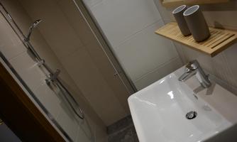 A modern bathroom with a shower and an elegant sink. On a wooden shelf, there are two gray cups.