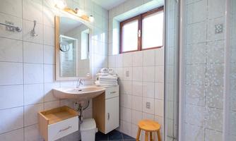 A modern bathroom with bright tiles and a sink. There is a shower, a stool, and fresh towels on a shelf.