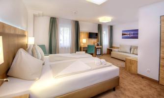 A modern room with two beds, a sofa, and plenty of natural light. The decor is bright and friendly, perfect for a relaxing stay.