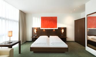 A modern bedroom with a double bed and minimalist decor. The walls are bright, and a red artwork adorns the wall above the bed.