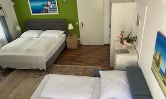A modern bedroom with two beds and a cozy atmosphere. The walls are painted green, and there are decorative pictures as well as fresh flowers on the table.
