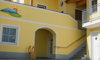 A yellow building with a seating area in front of the door. In the foreground, there is a wooden sled on snow.