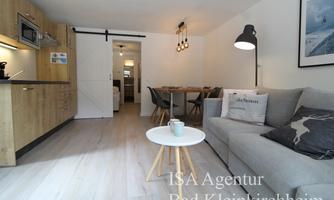 A modern holiday apartment with a cozy seating area and an open kitchen. The space is bright and inviting, perfect for a relaxing stay.