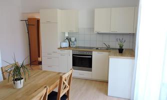 A modern kitchen with bright furniture and a dining area. The room is bright and friendly with a large window.