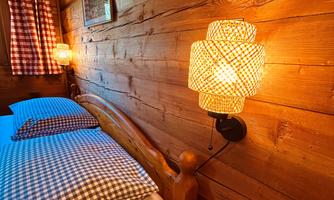A cozy bedroom with wood paneling. The bedding has a checked pattern and there is soft lighting from two wall lamps.