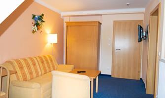 A cozy room with a sofa, a table, and a television. The walls are painted in soft colors, and there is a wardrobe as well as a lamp.