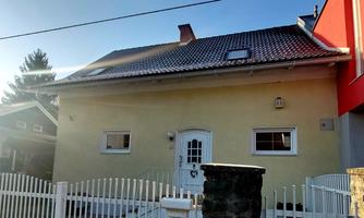 A yellow house with a white fence. The sky is clear and the garden looks well-maintained.