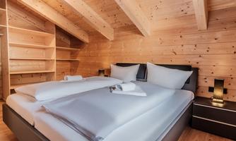 A cozy bedroom with a large bed and soft bedding. The wooden walls and ceiling structures give the room a warm atmosphere.