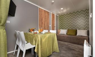 A modern living room with a table, chairs, and a cozy couch. There is a green tablecloth and fresh fruit on the table.