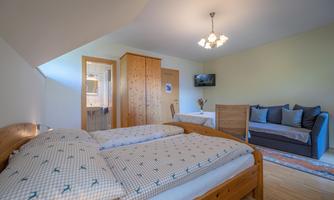 A cozy bedroom with a double bed and a seating area. The room is bright and friendly, with wood details and a television.