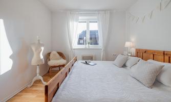 A bright bedroom with a large wooden bed and a cozy seating area. Natural light streams through the window, creating an inviting atmosphere.