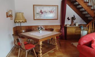 A cozy dining area with a wooden table and chairs. In the background, there is a staircase and a lamp.