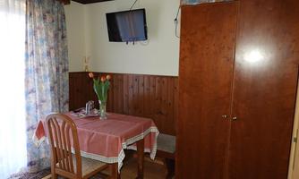 A cozy dining area with a table and chairs. A television hangs on the wall and there is a display case with flowers.