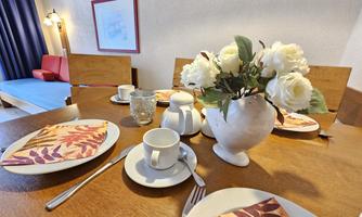 A beautifully set table with white roses in a vase. On the table are plates, cups, and napkins in autumn colors.