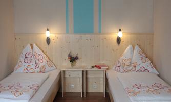 A cozy room with two single beds and modern wooden elements. The decorative cushions and a small flower vase give the room an inviting atmosphere.