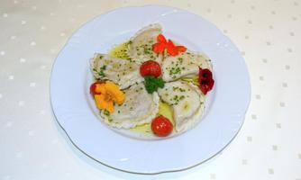 A plate with stuffed dumplings, garnished with cherry tomatoes and edible flowers. The dish is on a white plate and is drizzled with a herb oil sauce.