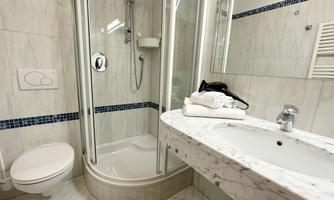 A modern bathroom with a shower cabin and a marble sink. Towels are neatly arranged on the shelf.