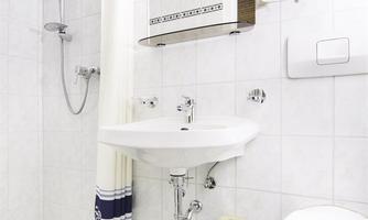 A modern bathroom with a shower, a sink, and a toilet. The walls are completely covered with tiles, and there are white towels.
