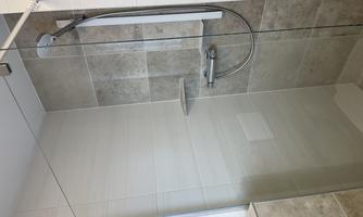 A modern shower with glass walls and a rain shower head. The walls are tiled in light, neutral colors.